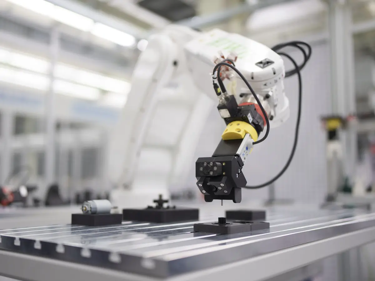 Industrieller Roboterarm mit Greifer positioniert ein Bauteil auf einem Montagetisch.