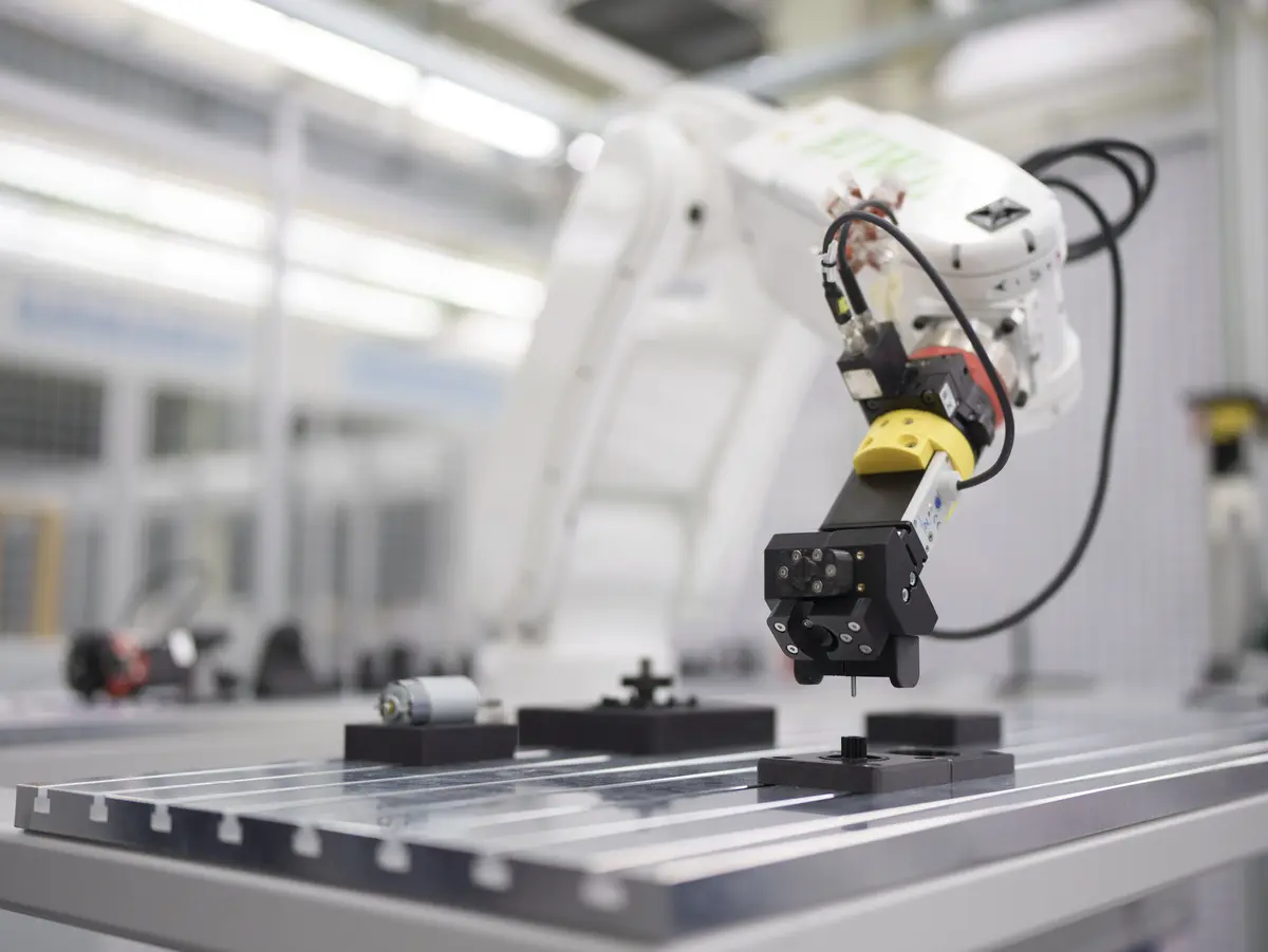 Industrial robotic arm with gripper positioning a component on an assembly table.
