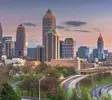 Skyline von Atlanta, USA, bei Sonnenuntergang mit beleuchteten Hochhäusern und fließendem Abendverkehr auf den geschwungenen Highways im Vordergrund.