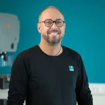 sutter-markus-sbikowski-ausbildungspate-feinmechanik.jpg Markus Sbikowski, Mitarbeiter der Produktion bei Sutter Medizintechnik, vor blauem Hintergrund – modernes Arbeitsumfeld und starke Teamkultur