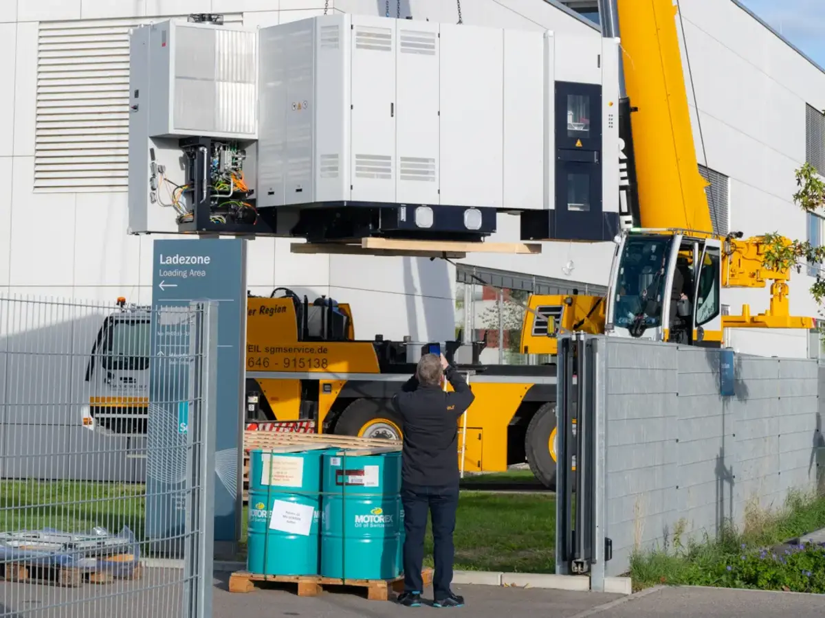 Mobile crane lifting large production equipment across an industrial facility for installation.