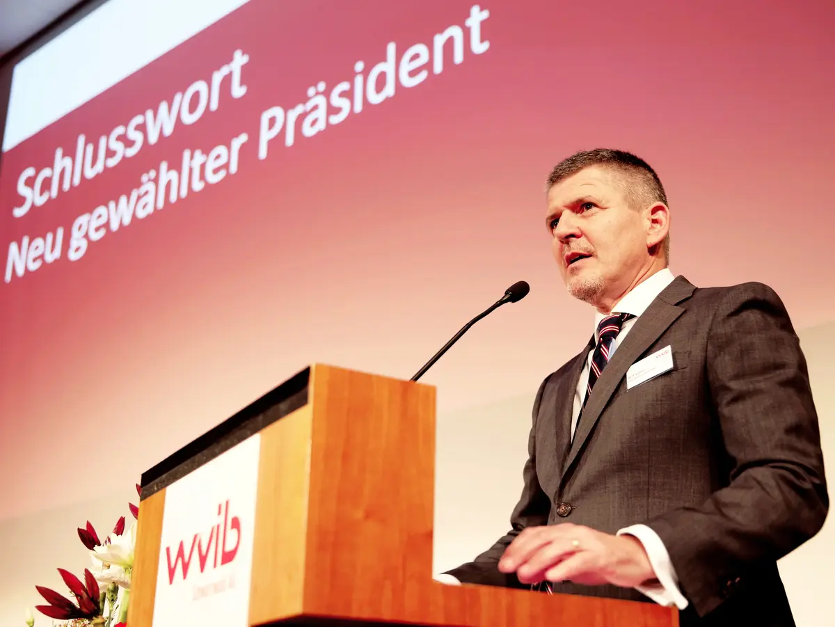 Person speaking at a podium on stage with a red presentation backdrop.