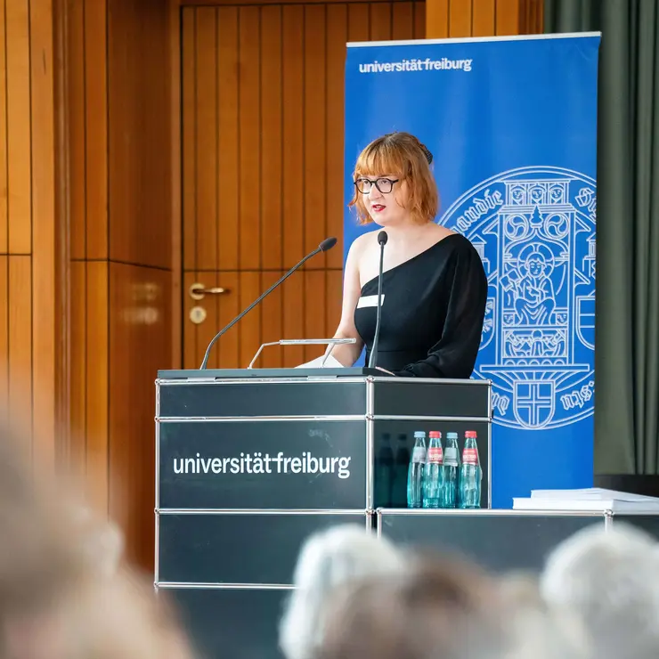 Person spricht an einem Rednerpult vor Publikum bei einer Veranstaltung der Universität Freiburg.
