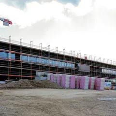 emmendingen-gebaeude-fassadenbau-2021.jpg Ansicht des Neubaus der Sutter Medizintechnik GmbH mit eingerüsteter Fassade, Kran und Baumaterialien auf dem Baugelände während der Fassadenarbeiten.