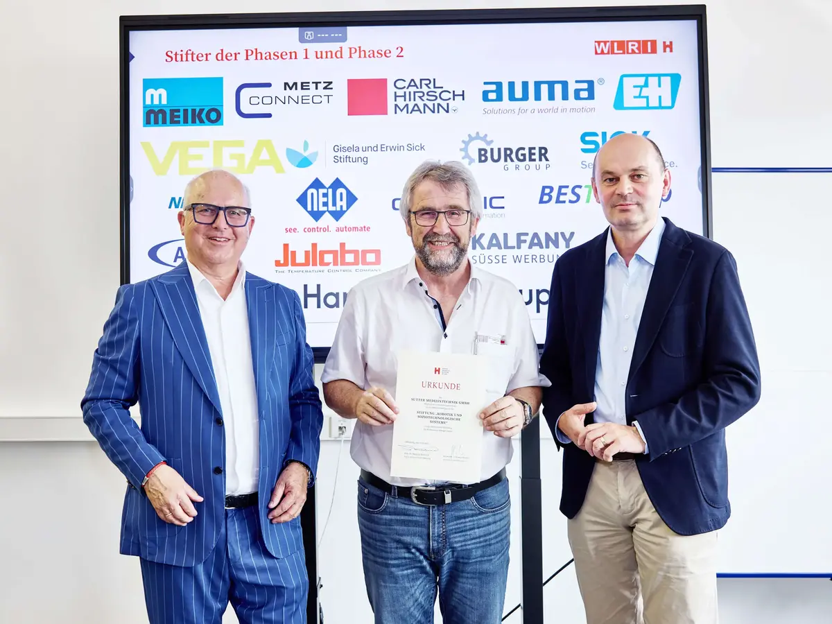 Drei Männer bei der Urkundenübergabe des WVIB Robotiktags 2025, im Hintergrund Sponsorenlogos auf einer Präsentationswand.