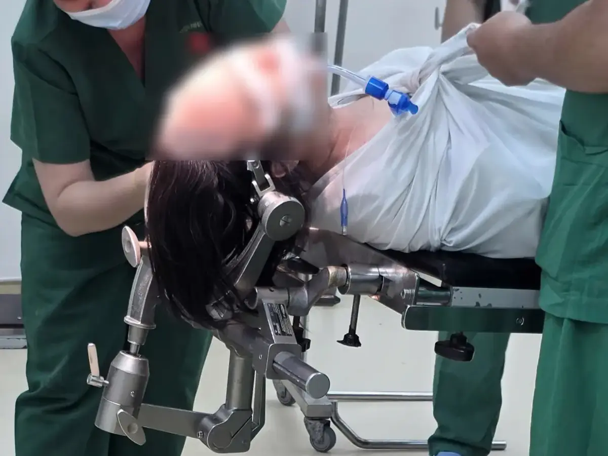 Medizinisches Personal lagert eine Patientin auf einem verstellbaren Operationstisch in einem klinischen Behandlungsraum.