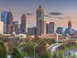 Skyline von Atlanta, USA, bei Sonnenuntergang mit beleuchteten Hochhäusern und fließendem Abendverkehr auf den geschwungenen Highways im Vordergrund.