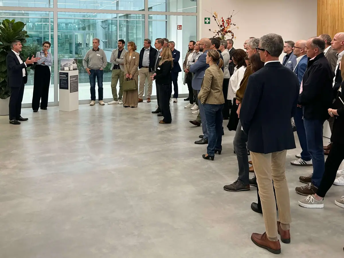 Eine größere Besuchergruppe steht im Foyer und hört einem Vortragenden im modernen Firmengebäude zu.