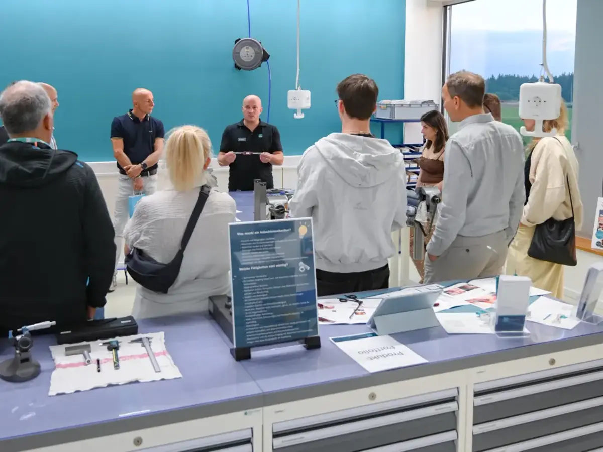 Besuchergruppe bei einer Führung durch die Lehrwerkstatt mit technischen Arbeitsplätzen und Maschinen.