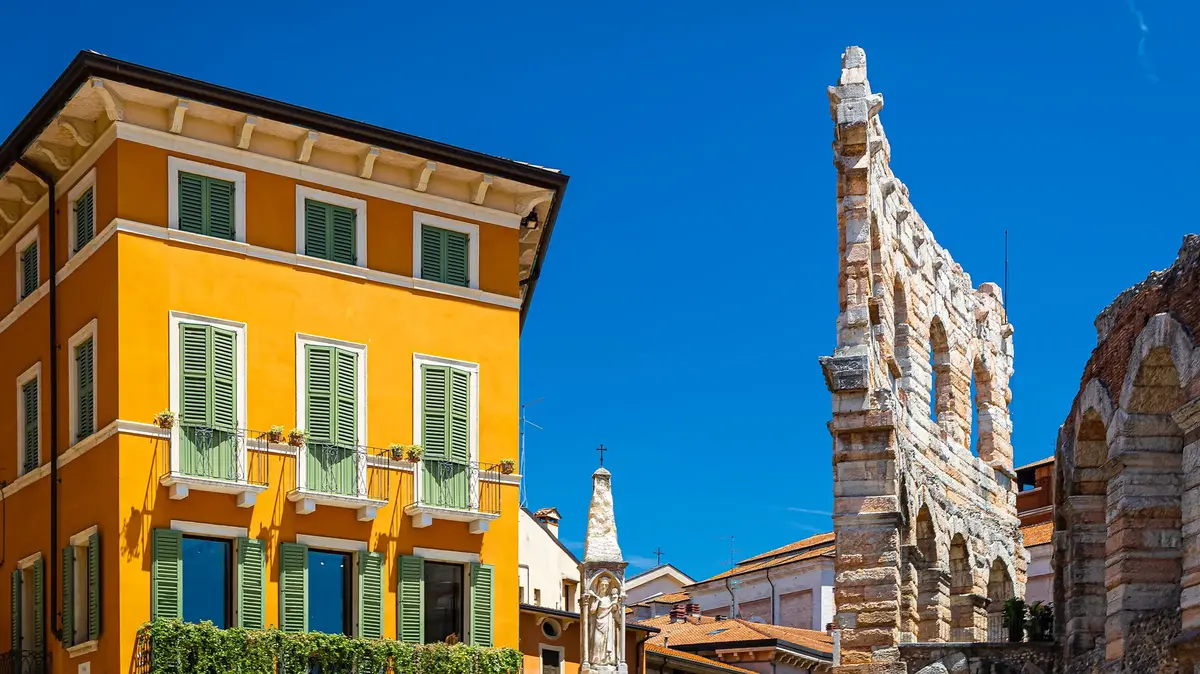 Historic Verona Arena beside yellow townhouse under a clear blue sky in Italy.