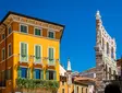 Historic Verona Arena beside yellow townhouse under a clear blue sky in Italy.