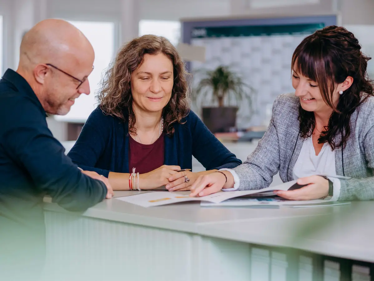 Drei Mitarbeitende im Kundenservice-Team besprechen gemeinsam Unterlagen bei einem Meeting im Büro.
