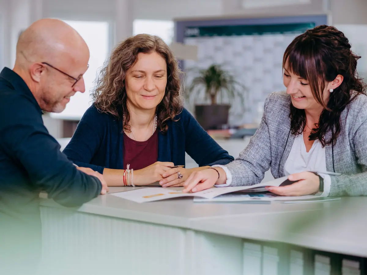 Drei Mitarbeitende im Kundenservice-Team besprechen gemeinsam Unterlagen bei einem Meeting im Büro.