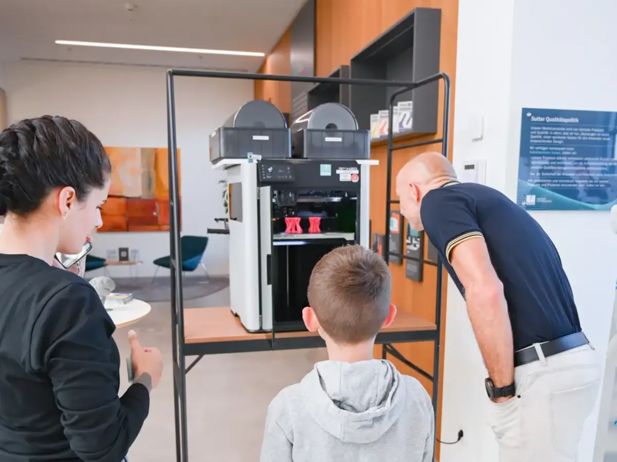Visitors watching a 3D printer during a live technology demonstration at a vocational training event.