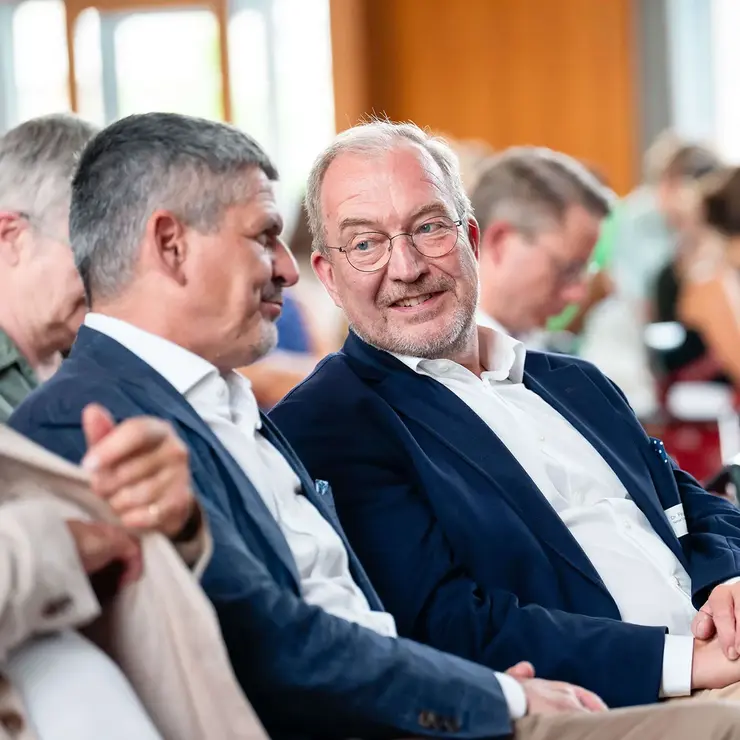 Attendees at a University of Freiburg event engaged in conversation before or during a program session. The image represents academic networking, collaboration, and dialogue between supporters, university representatives, and students.