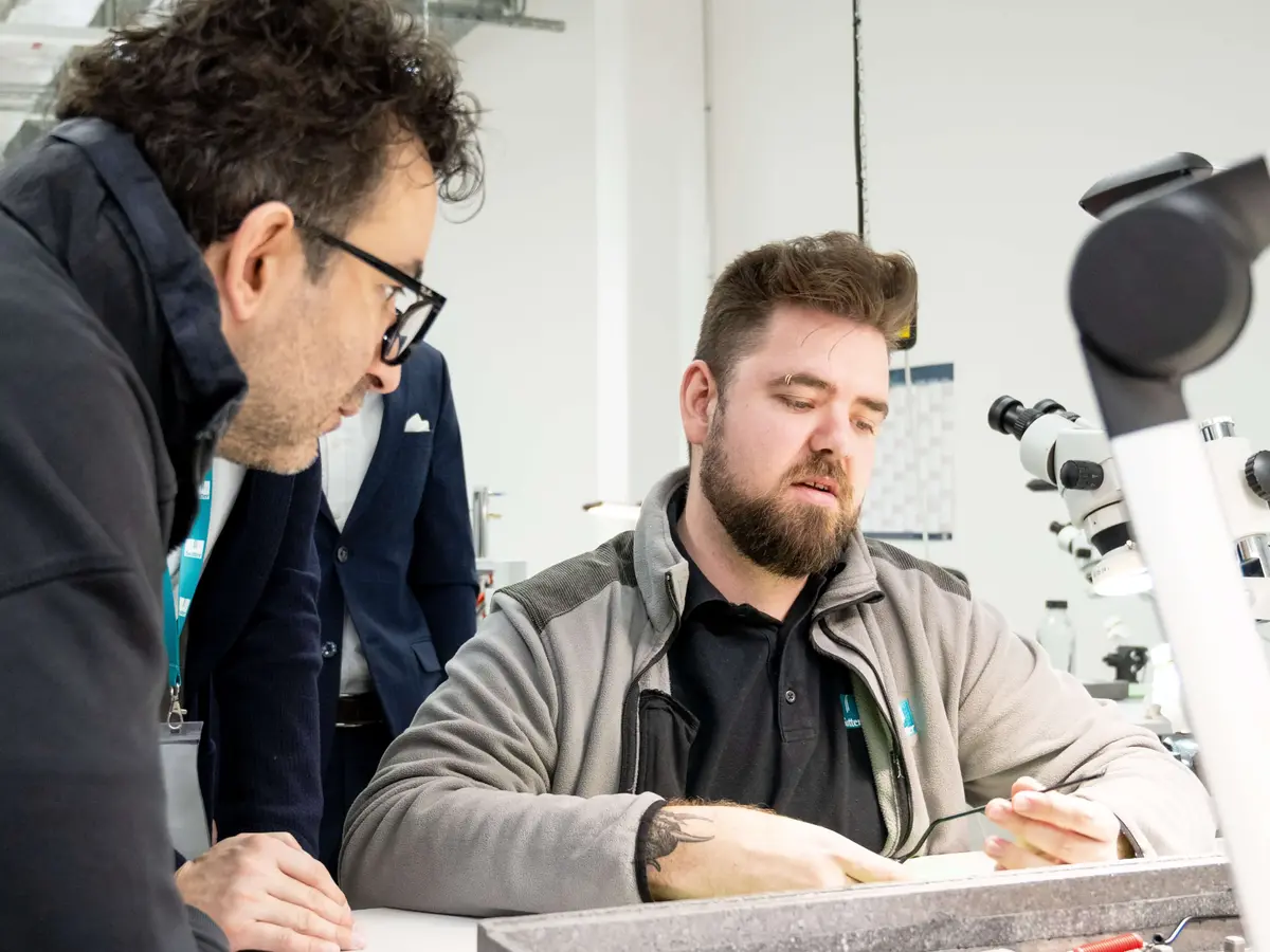 Two employees inspecting a component together at a workstation with a microscope in a technical environment