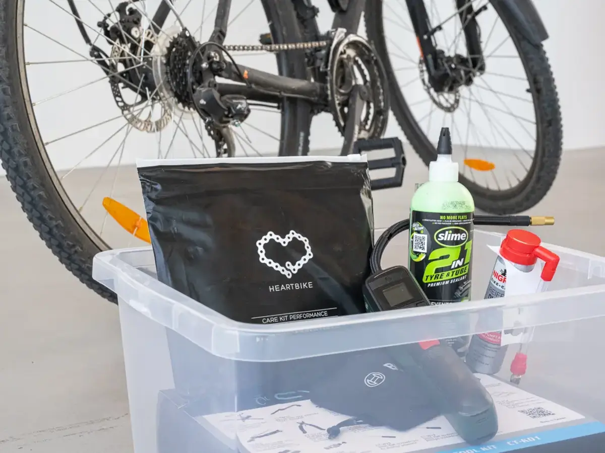 Bicycle component and accessories in a clear plastic storage box with a bicycle in the background.