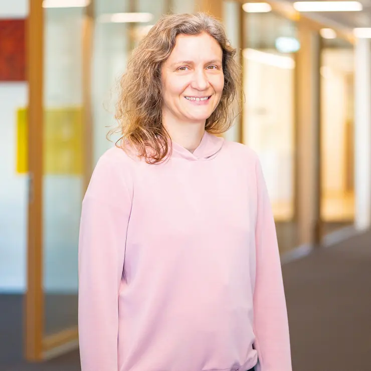 Frau mit lockigen, schulterlangen Haaren und rosa Hoodie steht im Flur von Sutter Medizintechnik und lächelt in die Kamera.