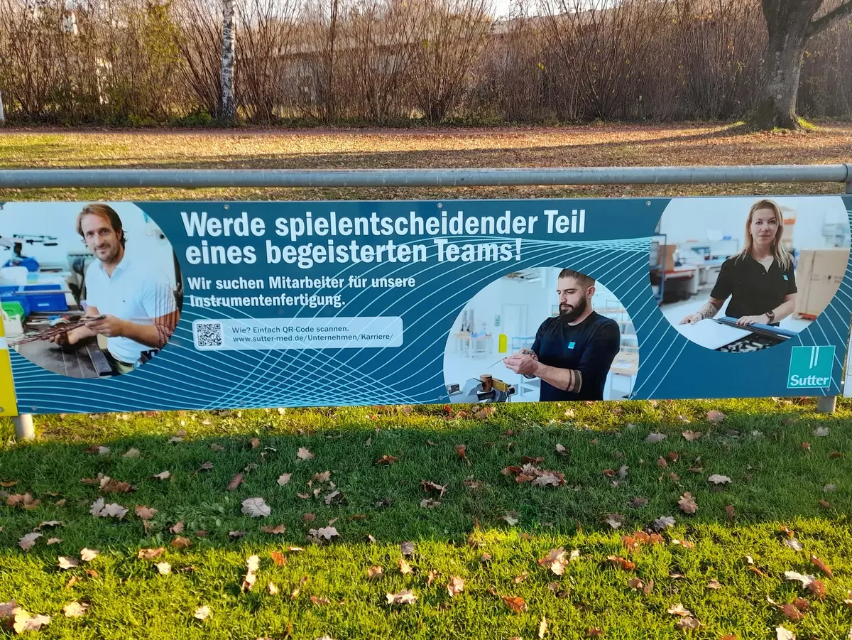 Recruiting-Banner mit Mitarbeitenden und Stellenaufruf für die Instrumentenfertigung im Außenbereich.