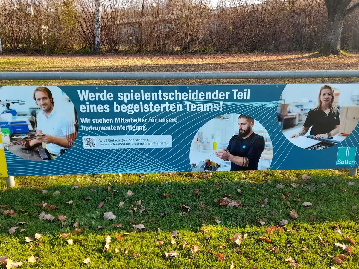 Outdoor recruitment banner featuring employees and a hiring message for instrument manufacturing positions.