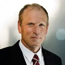 Prof. Dr. Kühnel im dunklen Anzug mit weißem Hemd und gestreifter Krawatte vor neutralem Hintergrund.