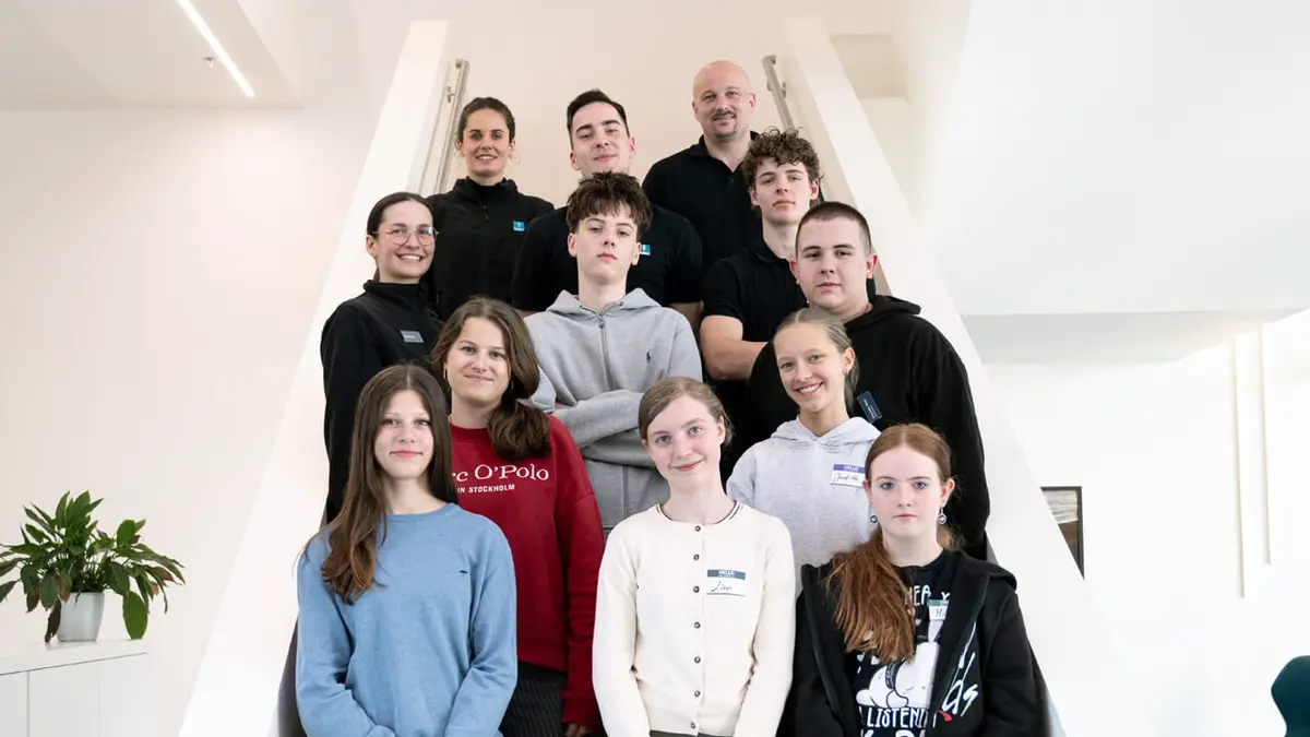 Group of approximately 15 people standing on a modern staircase in a bright indoor space.