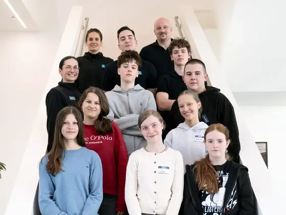 Gruppe von etwa 15 Personen steht auf einer modernen Treppe in einem hellen Innenraum.