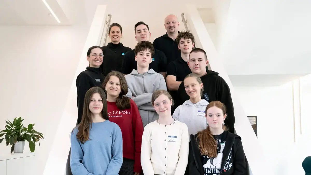 Gruppe von etwa 15 Personen steht auf einer modernen Treppe in einem hellen Innenraum.