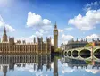 Palast von Westminster mit Big Ben und Spiegelung im Wasser an einem sonnigen Tag in London.