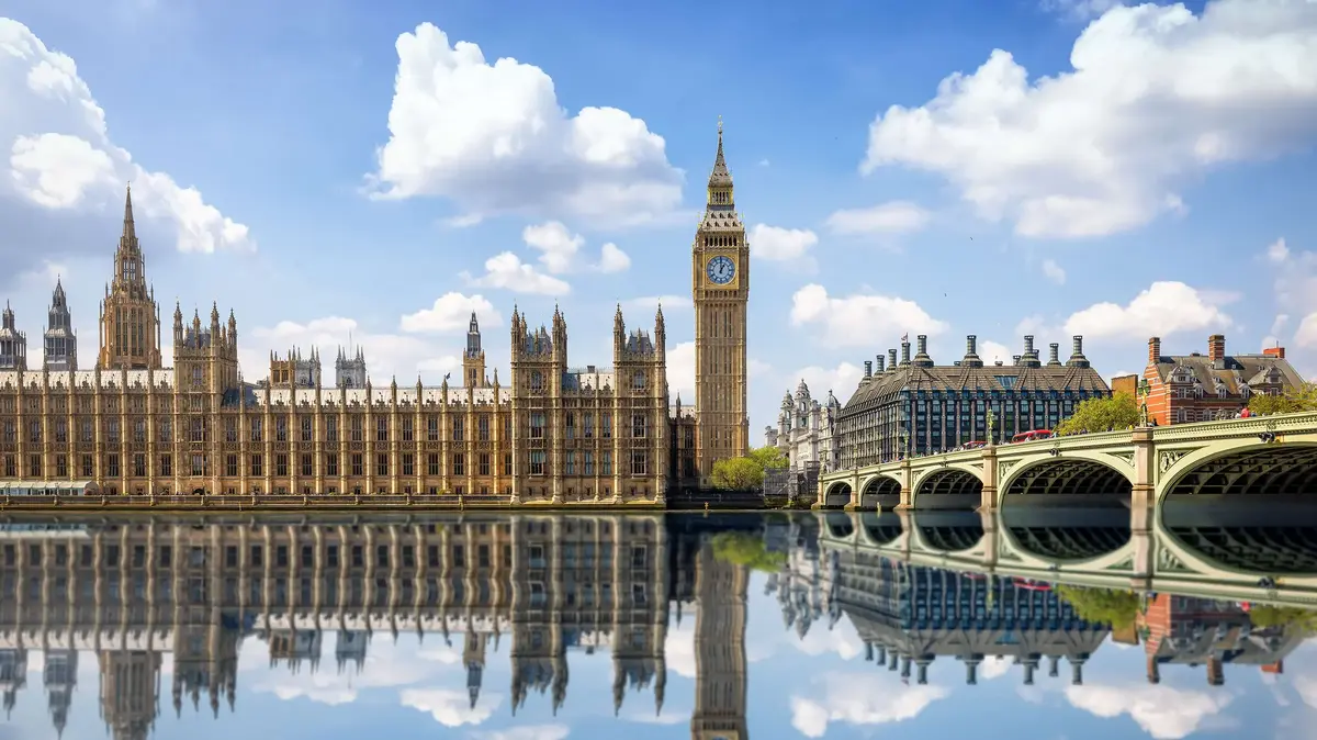 Palace of Westminster with Big Ben reflected in water on a sunny day in London.