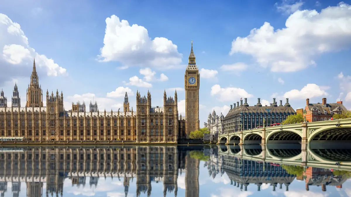 Palast von Westminster mit Big Ben und Spiegelung im Wasser an einem sonnigen Tag in London.