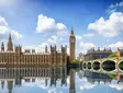 Palace of Westminster with Big Ben reflected in water on a sunny day in London.
