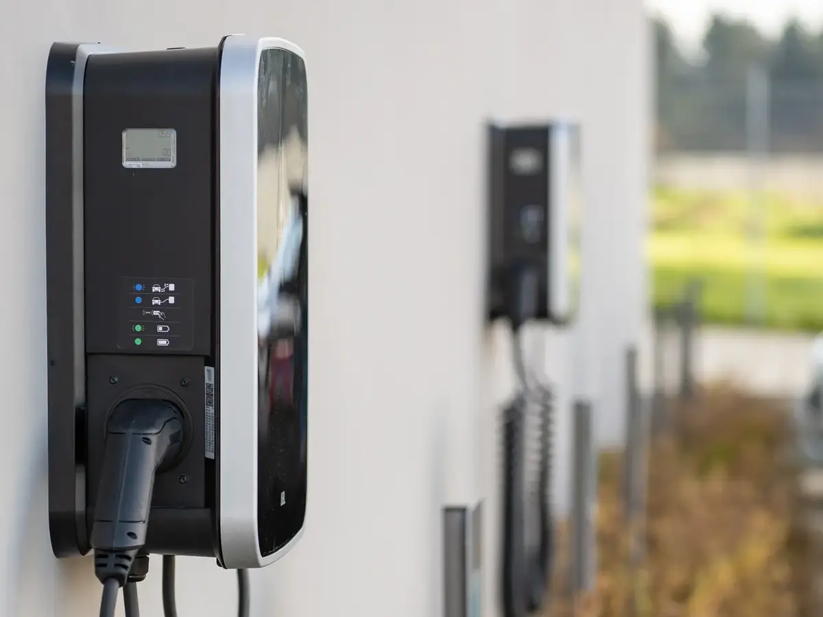 Mehrere Wallboxen für Elektroautos an einer Außenwand mit angeschlossenen Ladekabeln.