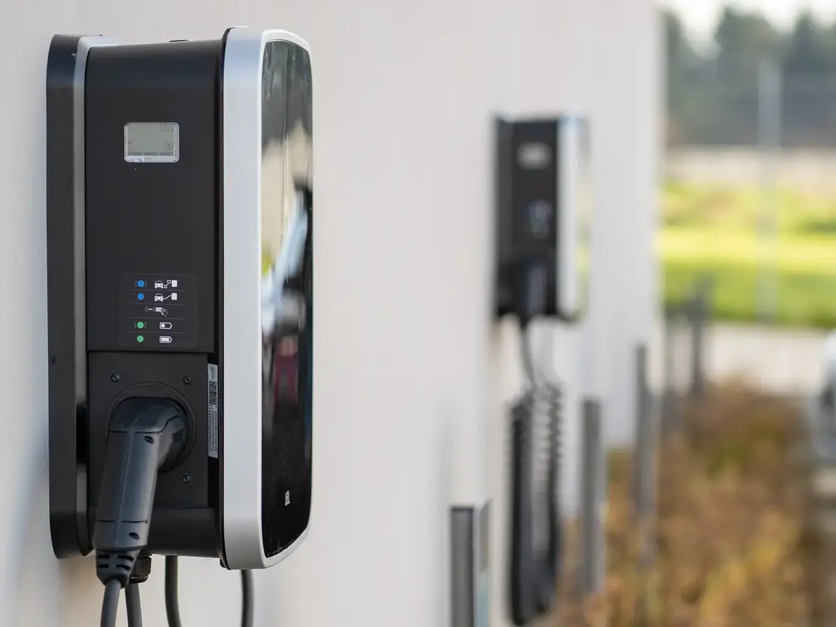 Multiple electric vehicle wall chargers mounted on an exterior wall with charging cables.