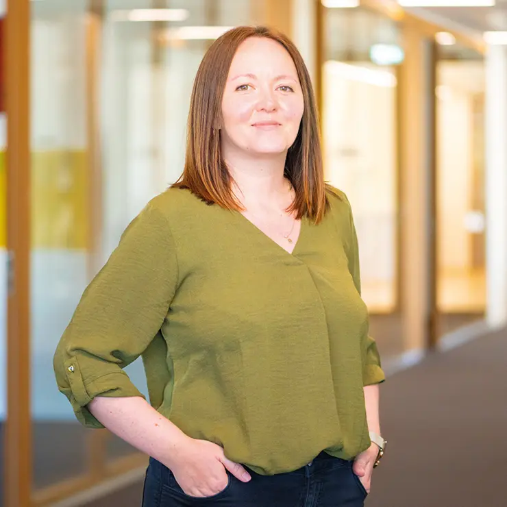 Eine Mitarbeiterin von Sutter Medizintechnik steht mit den Händen in den Hosentaschen im Büroflur und blickt selbstbewusst in die Kamera.