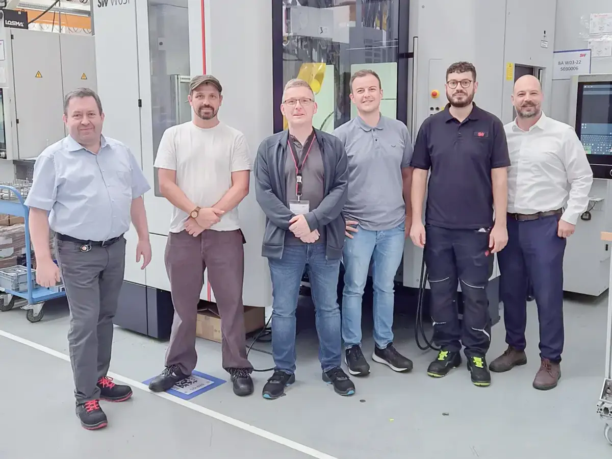 Mitarbeitende vor neuer CNC-Bearbeitungsmaschine in moderner Produktionshalle.