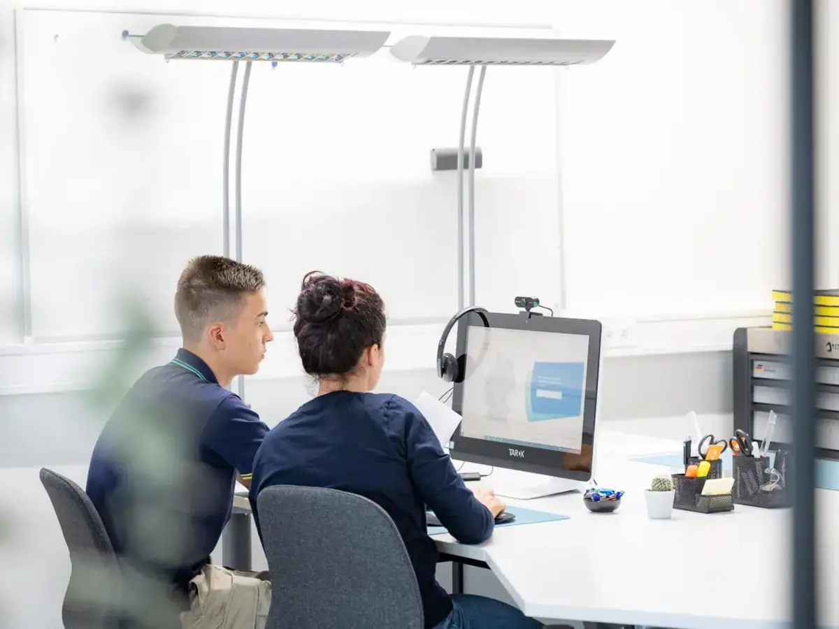 Two employees working together at a computer screen in a modern technical environment.