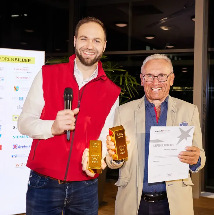 Two participants holding a certificate and a symbolic prize during an award ceremony.