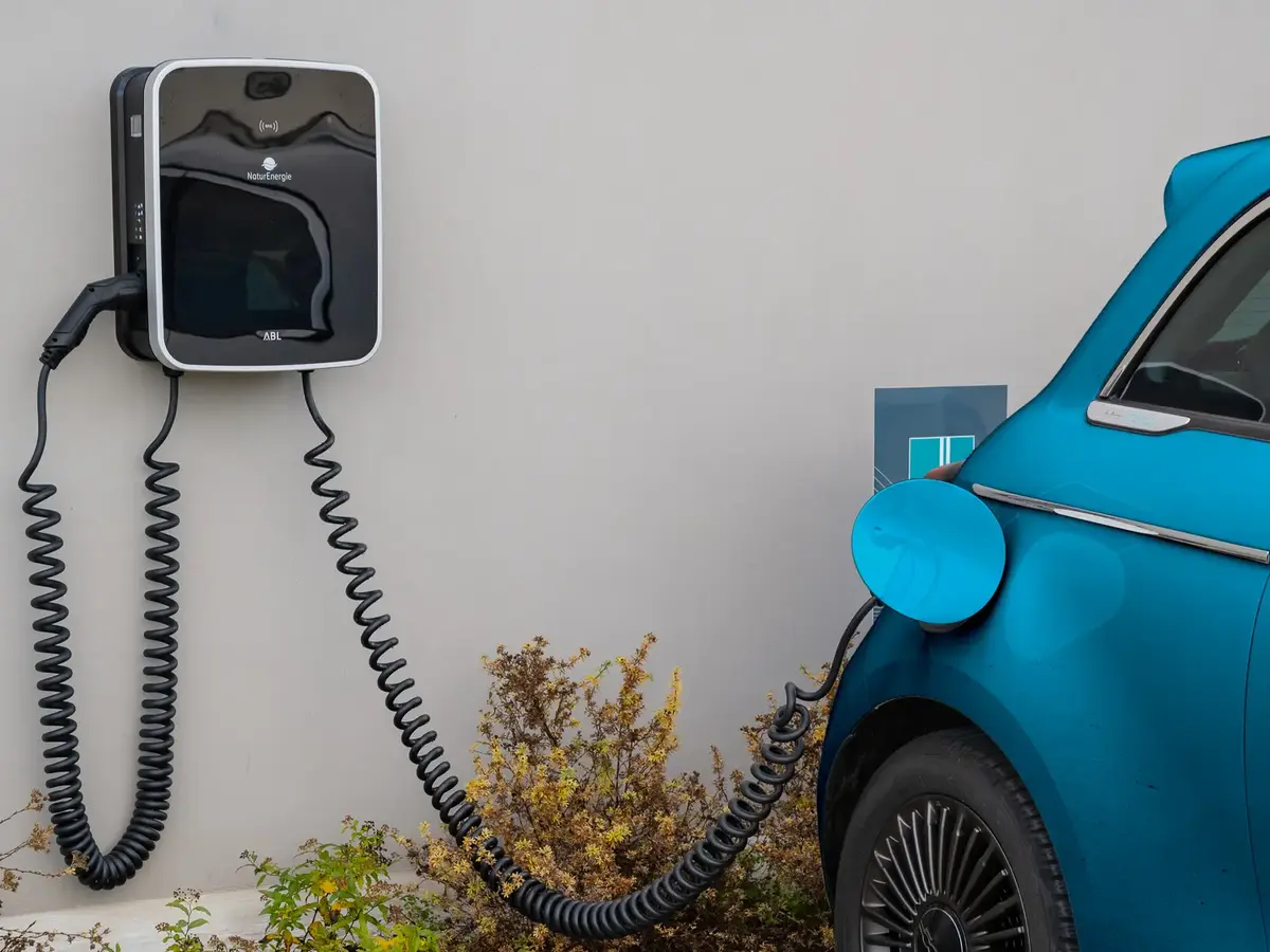 Blaues Elektroauto beim Laden an einer Wallbox vor einem Gebäude.