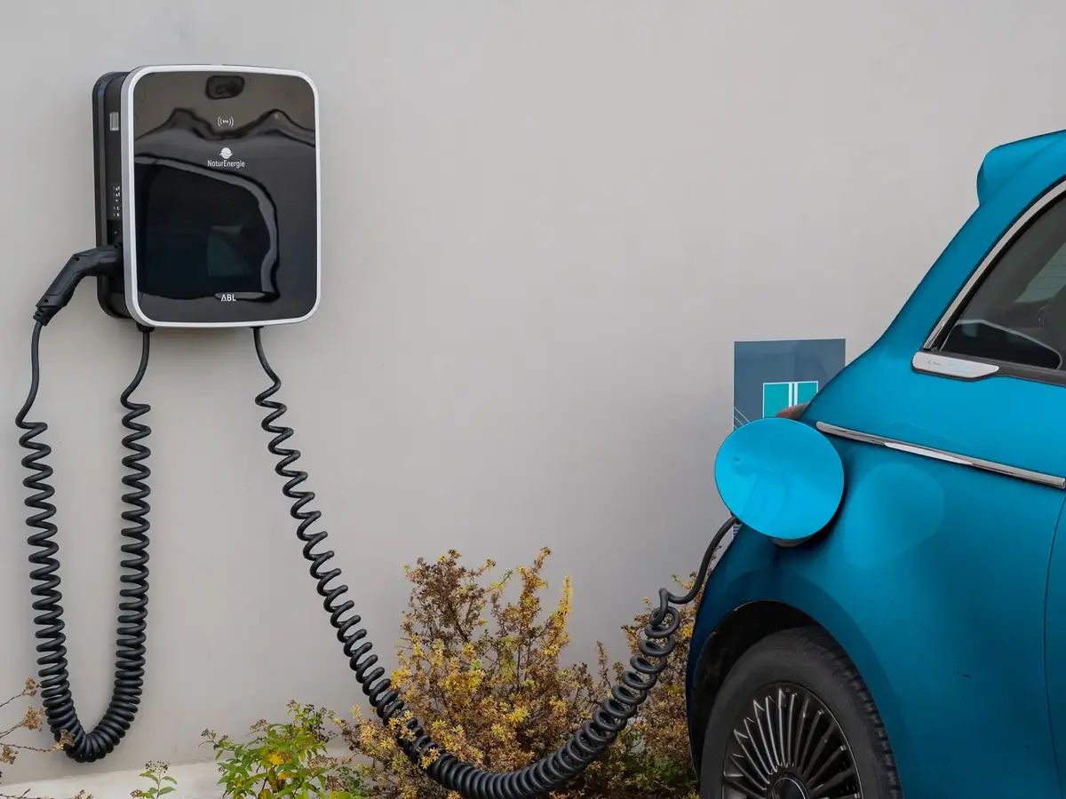 Blue electric vehicle charging at an outdoor wall-mounted charging station.