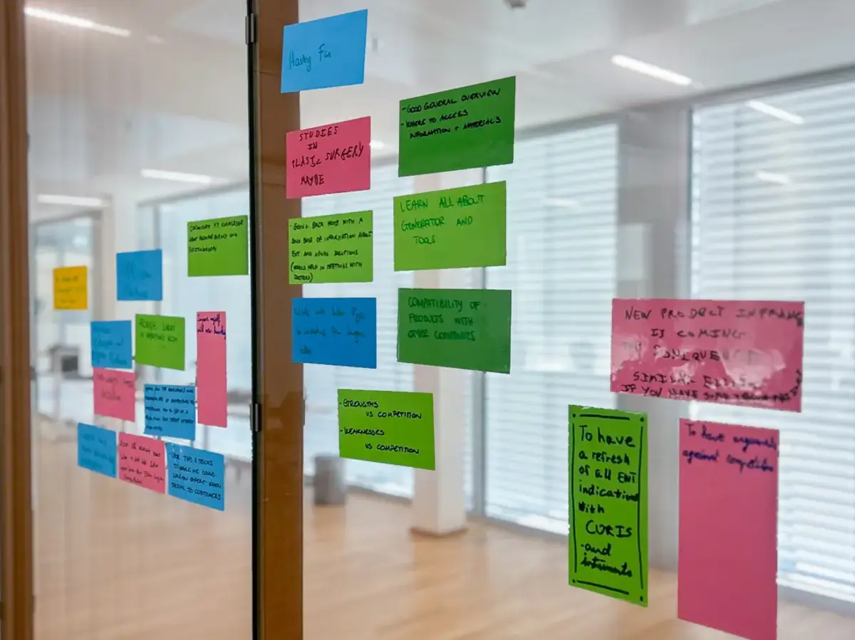 Workshop room with many colorful sticky notes arranged on a wall behind glass.