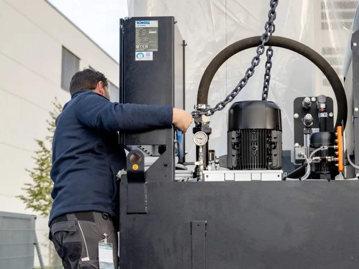 Worker attaching lifting chain to industrial machine during equipment installation.