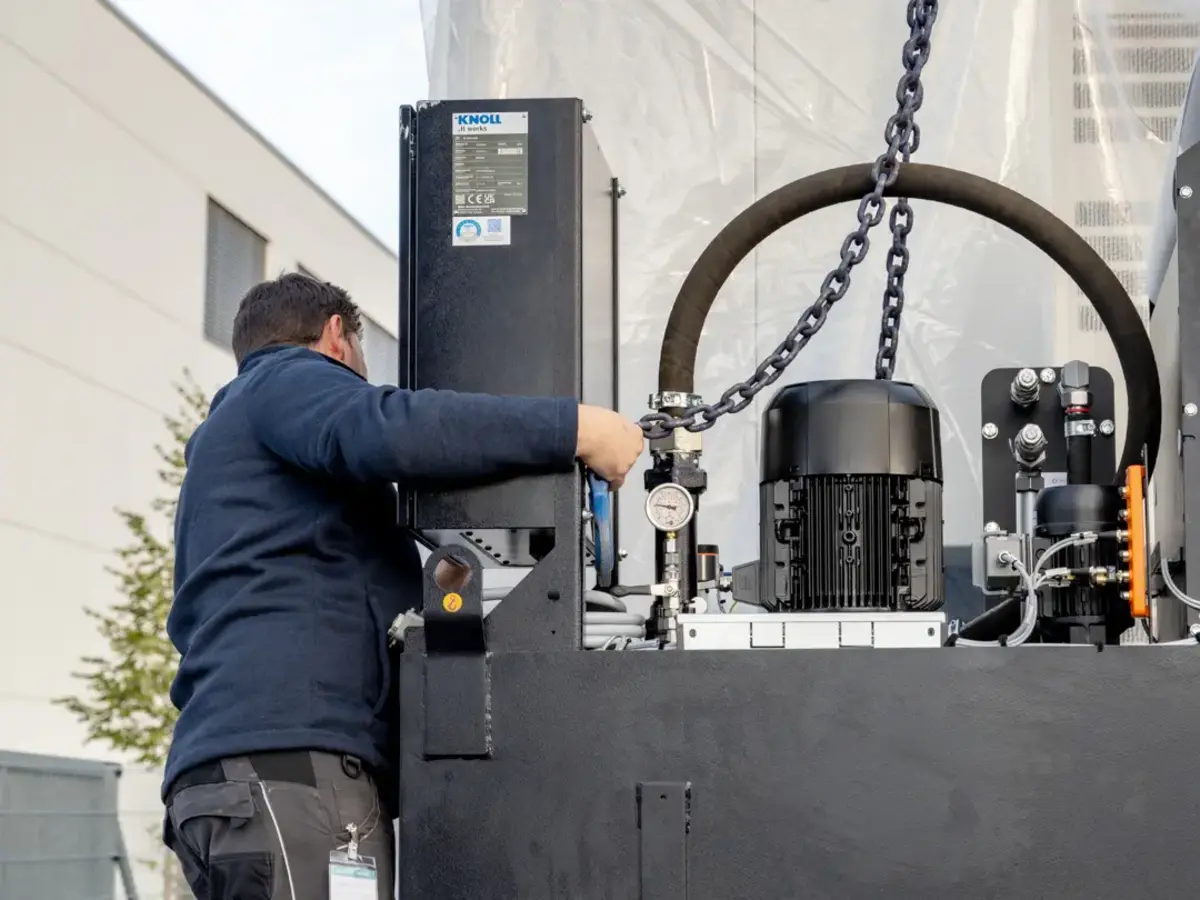 Mitarbeitender befestigt Hebekette an Industriemaschine während der Maschinenanlieferung.