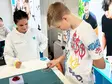 Eine Mitarbeiterin von Sutter Medizintechnik betreut einen Jungen am Messestand, der mit einer Pinzette kleine Kügelchen sortiert.