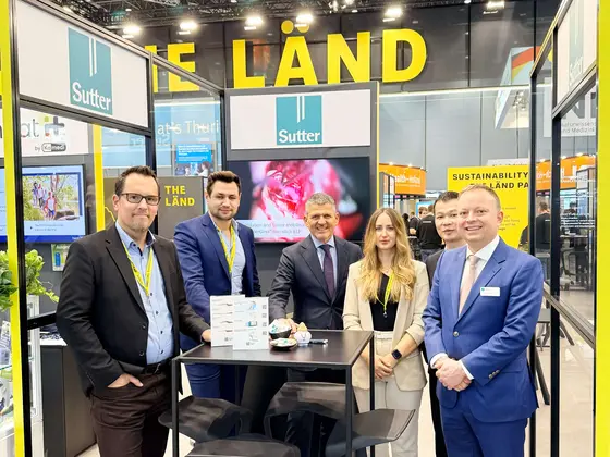 Messestand von Sutter Medizintechnik auf einer Fachmesse, mit fünf Personen vor einem Tisch, Unternehmenslogo sichtbar, umgeben von Bannern und Monitoren.