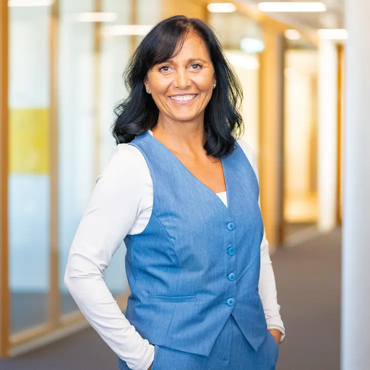 Lächelnde Frau mit dunklen Haaren im blauen Outfit steht im Flur von Sutter Medizintechnik – Team Empfang.