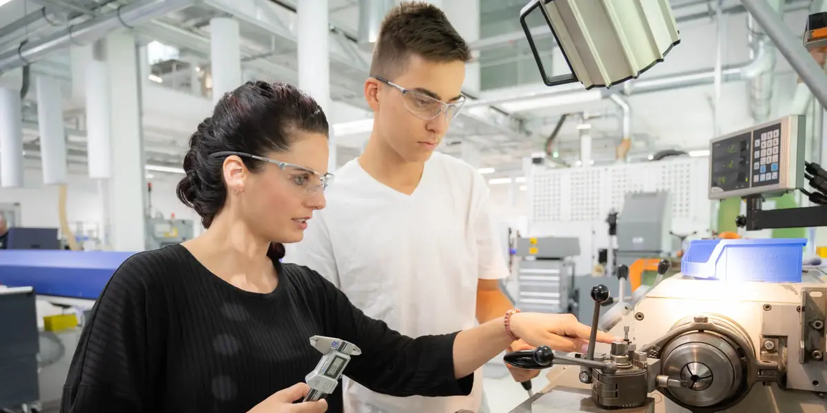 Franziska Beck, Ausbilderin bei Sutter Medizintechnik, zeigt einem Auszubildenden die Arbeit an der Drehmaschine – praxisorientierte Ausbildung.