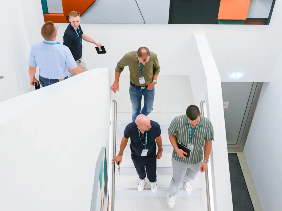 Mitglieder des Gewerbevereins Emmendingen besichtigen im Rahmen eines Unternehmensbesuchs die modernen Räumlichkeiten von Sutter Medizintechnik. Eine Gruppe bewegt sich durch ein helles Treppenhaus mit moderner Kunstinstallation.