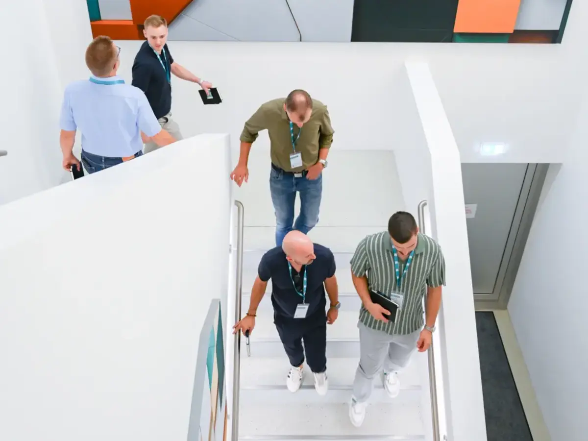 Members of the Emmendingen Business Association explore the modern facilities of Sutter Medical Technology during a company visit. A group walks through a bright stairwell featuring contemporary artwork.