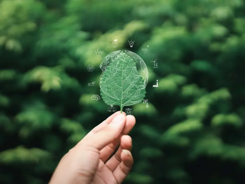 Hand hält grünes Blatt mit digital eingeblendeten Symbolen für Umweltschutz, CO₂-Reduktion und nachhaltige Technologien – Sinnbild für ökologische Innovation.